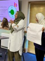 Two women presenting at a workshop holding up their findings (sticky notes) with a stage in the background