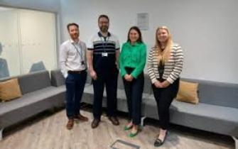 Four people standing up in front a light blue corner sofa networking
