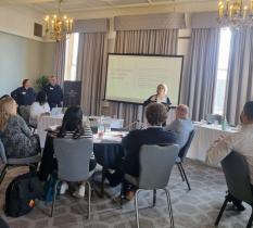 Workshop with people sat around circular tables watching a presenter against a large screen