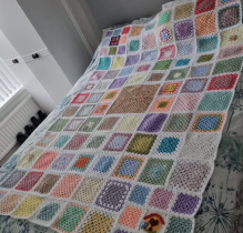 Large quilt made up of individual crocheted squares of different patterns and colours