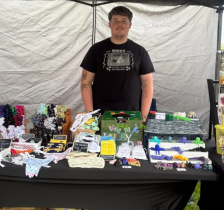 Picture of man standing behind a table displaying 3D printing gifts he is selling